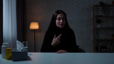 Karanlık dairede depresif bir kadın. Akıl sağlığı sorunları çeken bir kadın, kameranın önünde masada oturuyor, şaşırmış yüz ifadesi, olumsuz el hareketi, dur işareti yok..