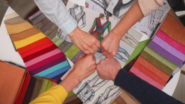 İş ekibi ofisinde toplanıyor. Yaratıcı moda ekibi üyeleri ve müşterileri toplantı masasında toplanıp yeni kıyafet tasarımı projesini tartıştılar. Takımın yumruk tokuşturma hareketi yaptılar..