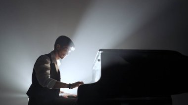 Klasik piyano konseri. Karanlık konser sahnesinde siyah piyanonun üzerinde oturan ve çalan piyanist, parlak spot ışıklarına karşı, siyah stüdyo arka planında izole edilmiş. Sanatçı konser salonunda gösteri yapıyor..