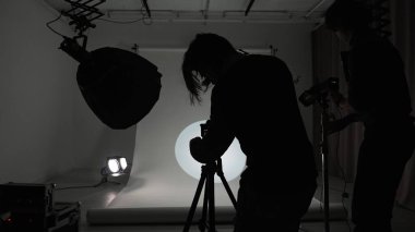 Profesyonel bir stüdyonun içinde. Modern ışıklandırma ekipmanlarıyla profesyonel çekim stüdyosu. Büyük beyaz siklonama, fotoğrafçı ve asistan. Işıklar ve kamera..