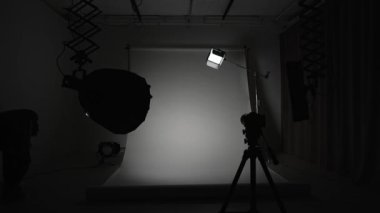 Profesyonel bir stüdyonun içinde. Modern ışıklandırma ekipmanlarıyla profesyonel çekim stüdyosu. Büyük beyaz siklonama arka planı. Işıkları ayarlayan fotoğrafçı ve kamera..