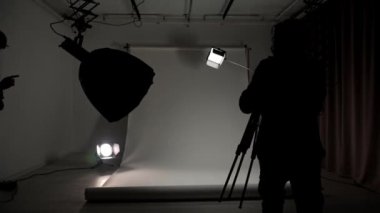 Profesyonel bir stüdyonun içinde. Modern ışıklandırma ekipmanlarıyla profesyonel çekim stüdyosu. Büyük beyaz siklonama, fotoğrafçı ve asistan. Işıklar ve kamera..