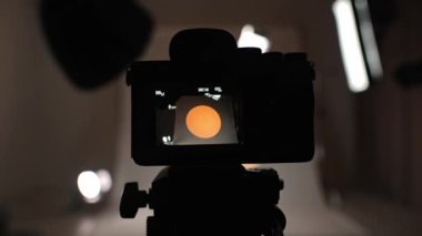 Profesyonel bir stüdyonun içinde. Profesyonel film stüdyosu ışıklandırma ve büyük siklonama arkaplanlı, kameradan tripoda canlı görüntü bulucu ekran, adam kamerayı açar.
