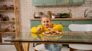Her gün aile hayatı ve çocuk bakımı. Anne ve kızı mutfakta, anne kıza zencefilli kurabiye yapmayı öğretiyor, küçük kız masada oturuyor ve kameraya gülümsüyor, tabakta kurabiyeler var.