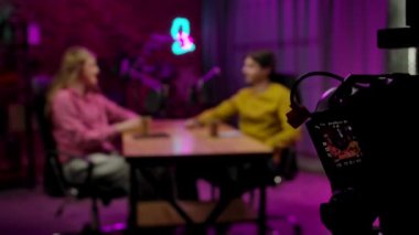 Çevrimiçi yayın. Sahne arkası bulanık ev sahibi ve konuk kayıt röportajı tavan arası podcast stüdyosunda, dijital içerik yaratıyor, tripodda çekim yapan kamera, pov. Yavaş çekim.