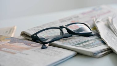 Bir gazeteye yakın plan gözlük. Masanın üzerinde siyah çerçeveli gözlüklerle duran bir gazeteyi gösteren bir fotoğraf..
