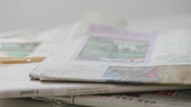 Gazetedeki gözlüklerin yakın çekimi. Siyah kare çerçeveli görüş gözlükleri yavaş çekimde bir yığın gazetenin üzerine düşüyor..
