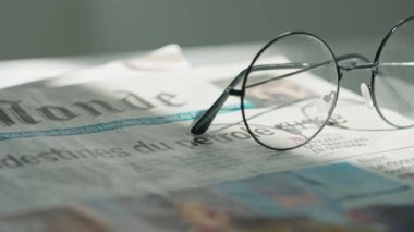 Gazetedeki gözlüklerin yakın çekimi. Üzerinde yuvarlak çerçeveli bardaklar olan bir gazetenin hareket halindeki görüntüsü..