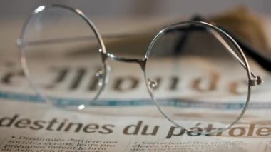 Gazetedeki gözlüklerin yakın çekimi. Üzerinde yuvarlak çerçeveli bardaklar olan bir gazetenin hareket halindeki görüntüsü..
