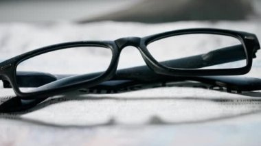 Gazetedeki gözlüklerin yakın çekimi. Üzerinde siyah kare çerçeveli görüş gözlüğü olan bir gazetenin hareket halindeki görüntüsü..