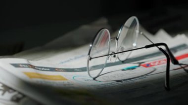 Gazetedeki gözlüklerin yakın çekimi. Üzerinde antika yuvarlak çerçeveli gözlüklerle bir masanın üzerinde duran gazetenin hareketli dairesel çerçevesi..