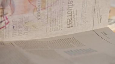 Masada dağınık bir gazete yığını var. Gazetenin sayfalarını çeviren ve parmağıyla doğru paragrafı gösteren bir adamın yan görüntüsü..