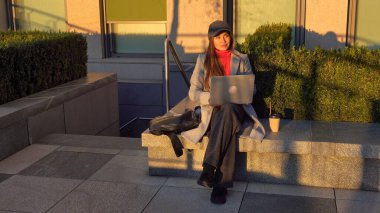 Dizüstü bilgisayarla çalışan şık bir genç kadın. Deri ceketli ve kepli bir kadın dizüstü bilgisayarında klavyede oturuyor. Megapolis 'te sonbahar günü.