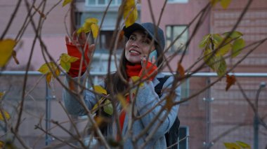 Akıllı telefondan konuşan şık bir genç kadın. Sıcak bir palto ve şapka giymiş bir kadın telefonda çok katlı bir şehir binasının arka planında sohbet ediyor..