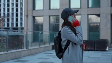 Akıllı telefondan konuşan şık bir genç kadın. Sıcak bir palto ve şapka giymiş bir kadın telefonda çok katlı bir şehir binasının arka planında sohbet ediyor..