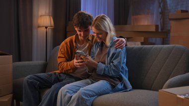 Genç bir adam ve bir kadın oturma odasında bir taşınma partisi hakkında konuşuyorlar. Birbirine aşık bir çift kanepede oturmuş, mutlu bir şekilde telefona bakıyor..