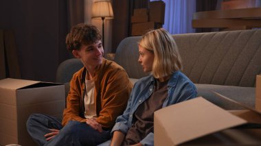 Genç bir adam ve bir kadın oturma odasında bir taşınma partisi hakkında konuşuyorlar. Birbirine aşık bir çift yerde oturuyor, koltuğun yastıklarını kutulardan çıkarıyorlar..