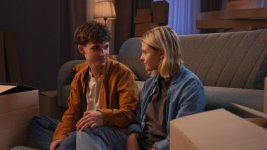 Genç bir adam ve bir kadın oturma odasında bir taşınma partisi hakkında konuşuyorlar. Birbirine aşık bir çift yerde oturuyor, koltuğun yastıklarını kutulardan çıkarıyorlar..