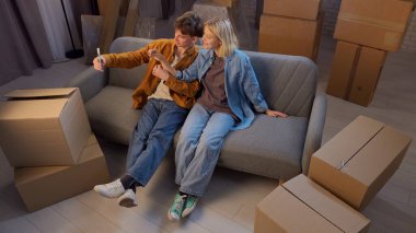 Genç bir adam ve bir kadın oturma odasında bir taşınma partisi hakkında konuşuyorlar. Birbirine aşık bir çift kanepeye oturur ve ev şeklinde anahtarlıklarla kendi fotoğraflarını çekerler..