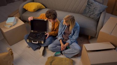 Genç bir adam ve bir kadın oturma odasında bir taşınma partisi hakkında konuşuyorlar. Birbirine aşık bir çift yerde oturuyor, kız vinil plak çalar şeklinde bir hediye veriyor..