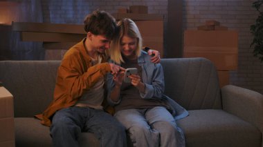 Genç bir adam ve bir kadın oturma odasında bir taşınma partisi hakkında konuşuyorlar. Birbirine aşık bir çift kanepede oturmuş, mutlu bir şekilde telefona bakıyor..