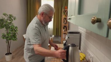 Son sınıf öğrencisinin hayatında bir gün. Yaşlı gri saçlı adam sabah mutfakta, adam sağlıklı kahvaltı hazırlıyor, yulaf taneleriyle su koyuyor. Günlük rutin yaşam tarzı kavramı.