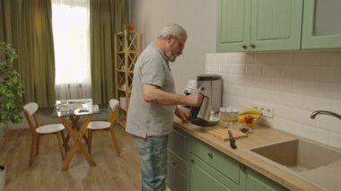 Son sınıf öğrencisinin hayatında bir gün. Yaşlı gri saçlı adam sabah mutfakta, adam sağlıklı kahvaltı hazırlıyor, yulaf taneleriyle su koyuyor. Günlük rutin yaşam tarzı kavramı.