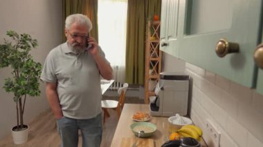 Son sınıf öğrencisinin hayatında bir gün. Yaşlı gri saçlı adam sabah mutfakta, adam akıllı telefonla konuşuyor ve sağlıklı kahvaltı hazırlıyor. Günlük rutin yaşam tarzı kavramı.