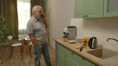 Son sınıf öğrencisinin hayatında bir gün. Yaşlı gri saçlı adam sabah mutfakta, adam akıllı telefonla konuşuyor ve sağlıklı kahvaltı hazırlıyor. Günlük rutin yaşam tarzı kavramı.