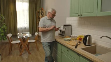 Son sınıf öğrencisinin hayatında bir gün. Yaşlı gri saçlı adam sabah mutfakta, akıllı telefondan mesaj atan adam, uygulamayla mesaj yollayan, günlük yaşam tarzı konsepti.