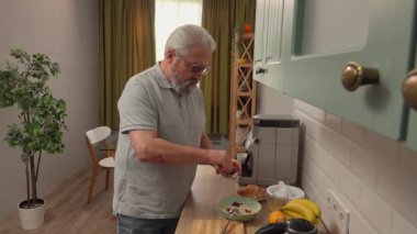 Son sınıf öğrencisinin hayatında bir gün. Yaşlı gri saçlı adam sabah mutfakta, adam sağlıklı kahvaltı hazırlar, yulaflı meyve ve böğürtlen ekler. Günlük rutin yaşam tarzı kavramı.