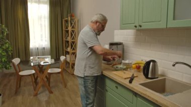 Son sınıf öğrencisinin hayatında bir gün. Yaşlı gri saçlı adam sabah mutfakta, adam sağlıklı kahvaltı hazırlar, yulaflı meyve ve böğürtlen ekler. Günlük rutin yaşam tarzı kavramı.