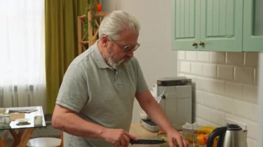 Son sınıf öğrencisinin hayatında bir gün. Yaşlı gri saçlı adam sabah mutfakta, sağlıklı kahvaltı hazırlıyor, muz kesiyor ve yulaf ezmesiyle kaseye ekliyor, pozitif ifade. Günlük rutin yaşam tarzı kavramı