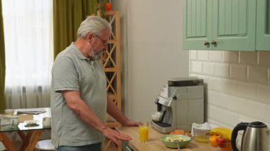 Son sınıf öğrencisinin hayatında bir gün. Yaşlı gri saçlı adam sabah mutfakta kahvaltı hazırlıyor, portakal suyu bardakta ve kahve makinesinden kahve bekliyor. Günlük rutin yaşam tarzı kavramı.