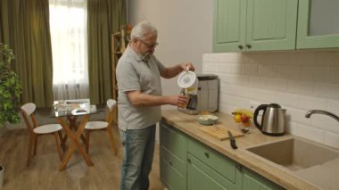 Son sınıf öğrencisinin hayatında bir gün. Yaşlı gri saçlı adam sabah mutfakta kahvaltı hazırlıyor, portakal suyu bardakta ve kahve makinesinden kahve bekliyor. Günlük rutin yaşam tarzı kavramı.
