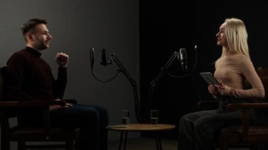 Çevrimiçi podcast gösterisi. Erkek sunucu ve kadın konuk kayıt röportajı şık podcast stüdyosunda mikrofonlarla, dijital içerik yaratarak, sunucu konuşan kadın soruları tablet kullanarak cevaplıyor..