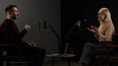 Çevrimiçi podcast gösterisi. Erkek sunucu ve kadın konuk kayıt stüdyosunda mikrofon kullanarak, dijital içerik yaratarak, sunucu misafirlerle konuşarak ve beşlik çakarak, olumlu ifade vererek röportaj yapıyorlar..