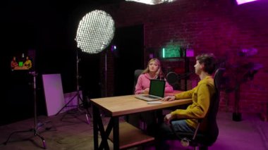 Çevrimiçi yayın. Erkek sunucu ve kadın misafir kayıt stüdyosunda mikrofon kullanarak, konuşarak dijital içerik yaratarak, krom anahtar yeşil ekran modeliyle dizüstü bilgisayar kullanarak röportaj yaparken sahne arkası görüntüsü..