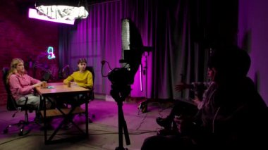 Çevrimiçi yayın. Çatı katındaki podcast stüdyosunda sahne arkası görüntüsü, erkek sunucu ve kadın konuk konuk konuşmaları, kayıt bitimi ve veda etme, kameraman ve yapımcı kontrol süreci.