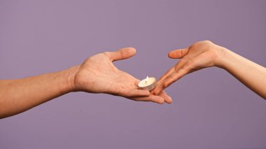 El hareketleri ve işaretleri. Erkek ve kadın el ele tutuşuyor, kadın erkeğe mum yakıyor, mor stüdyo arka planında izole edilmiş, yakın çekim. Sevgililer Günü reklam konsepti.