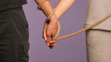 Hand gestures and signs. Man hand tied with rope, woman holding his hand, abusive dominated feministic relationships concept, isolated on purple studio background, close up shot. clipart