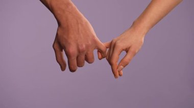 El hareketleri ve işaretleri. Erkek ve kadın el ele tutuşuyor, serçe parmaklarıyla dokunuyor, kilit altında, mor stüdyo arka planında izole edilmiş, yakın çekim. Sevgililer Günü reklam konsepti.