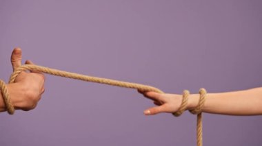 El hareketleri ve işaretleri. Erkek ve kadın elleri birbirine bağlanmış, halatla birbirine dolanmış, taciz ya da birbirine bağımlı ilişkiler konsepti, mor stüdyo arka planında izole edilmiş, yakın çekim.