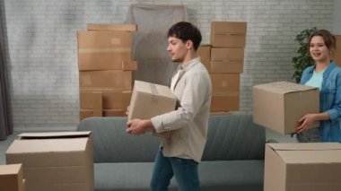 Yeni eve taşınma konsepti. Genç bir çift yeni bir daireye taşınıyor, yer karton kutularla dolu, erkek ve kadın yeni bir daireye kutular ile geliyorlar, etrafa bakınıyorlar, mutlu ve pozitif bir ifade..