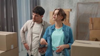 Yeni eve taşınma konsepti. Genç çift yeni daireye taşınıyor, yer karton kutularla dolu, erkek ve kadın odada duruyor, konuşuyor ve yeni dairenin yenilenmesini tartışıyorlar, pozitif ifade.