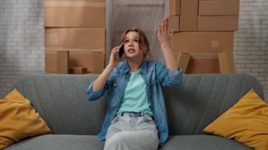 Yeni eve taşınma konsepti. Yeni daireye taşınan genç bir çift, karton kutularla dolu bir yer, akıllı telefondaki yeni apartman sohbetlerinin olduğu koltukta oturan bir kadın, hayal kırıklığına uğramış olumsuz ifade..