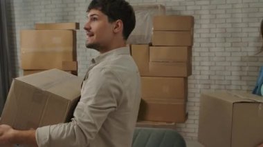 Yeni eve taşınma konsepti. Genç çift yeni bir daireye taşınıyor, yer karton kutularla dolu, erkek ve kadın yeni bir daireye kutular ile giriyor, etrafına bakınıyor, heyecanlı ve pozitif ifade.