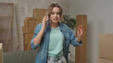 Yeni eve taşınma konsepti. Genç çift yeni daireye taşınıyor, yer karton kutularla dolu, kadın yeni dairenin odasında duruyor ve akıllı telefondan konuşuyor, hayal kırıklığına uğramış olumsuz ifade..