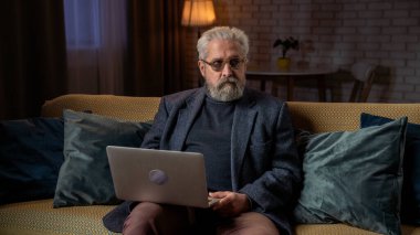 Son sınıf öğrencisinin hayatında bir gün. Yaşlı gri saçlı adam akşam vaktini evde geçiriyor oturma odasında kanepede oturuyor, dizüstü bilgisayarda çalışıyor ve başka tarafa bakıyor. Günlük rutin yaşam tarzı kavramı.