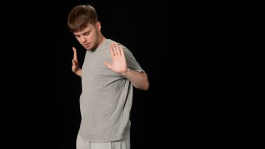 Açık gri elbiseli genç adam siyah arka planda hip-hop yapıyor..